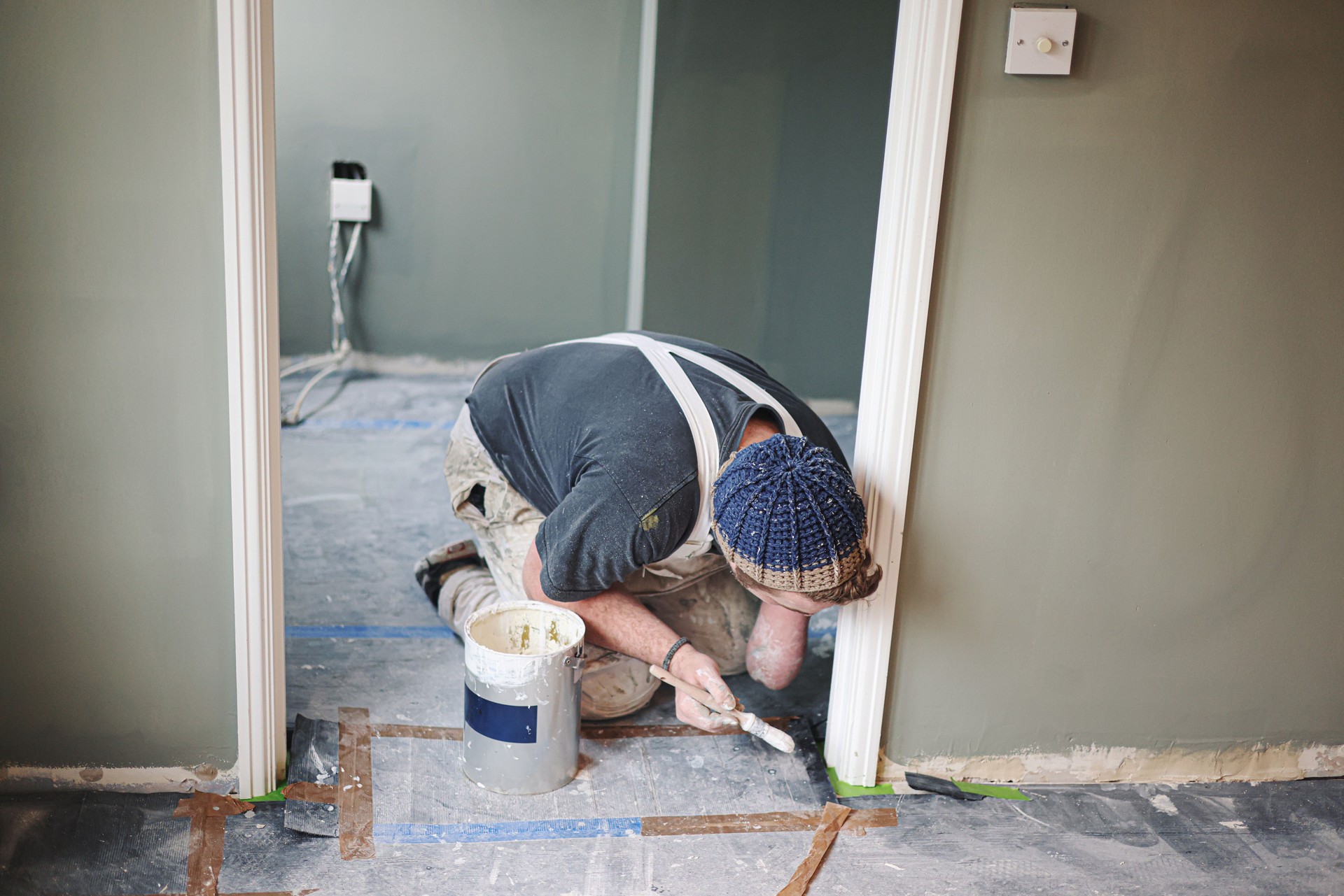 Young, skilled Painter & Decorator overcoming the disability of having one hand as he carefully and skilfully paints a door architrave in a residential house